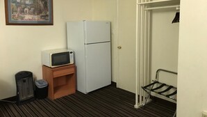 A small, compact room with a white refrigerator, a microwave on a wooden shelf, a trash bin, and a coat rack. - Blue Mountain Hotel (Dayton)