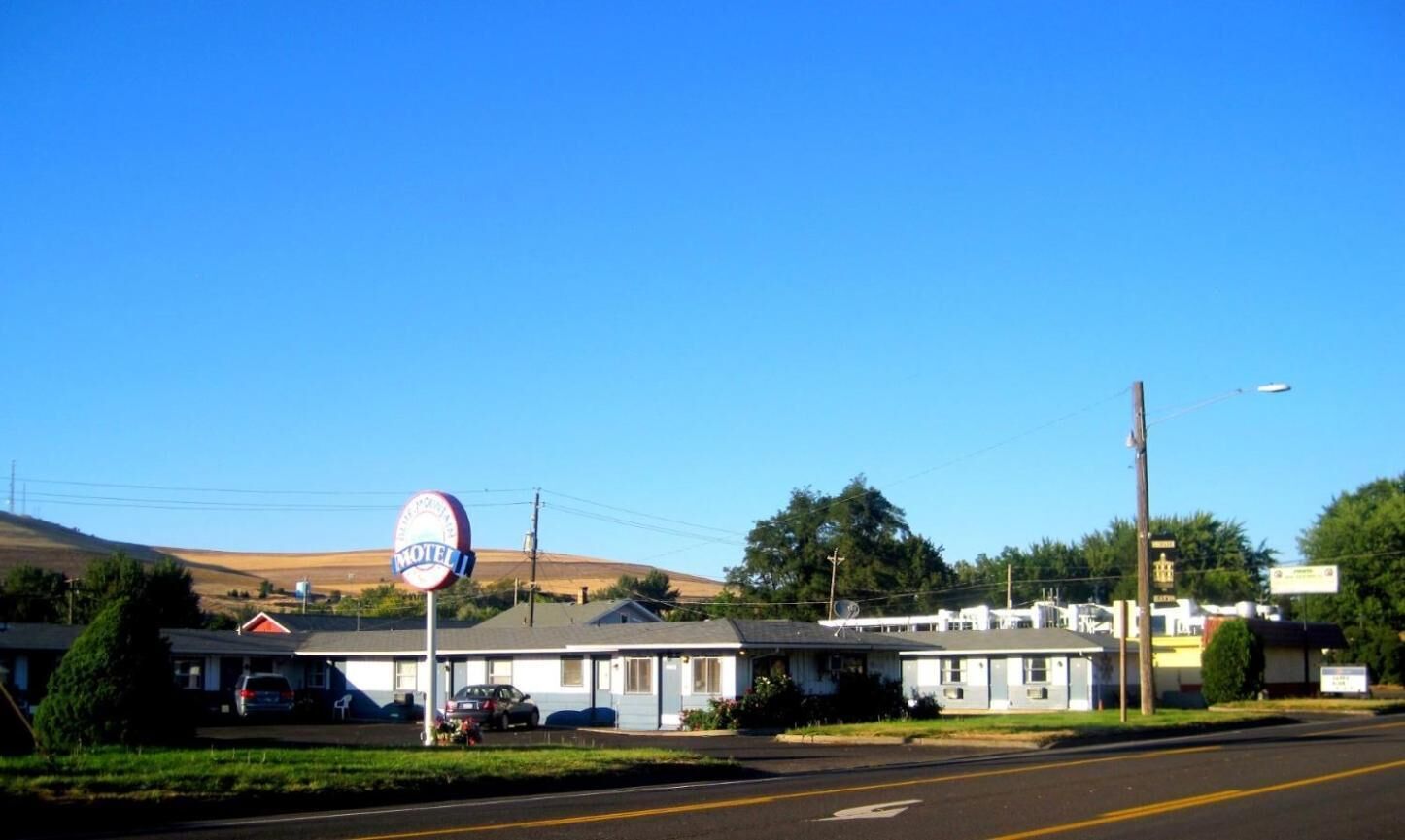 A motel with a single-story building, a parking lot, and a clear blue sky.