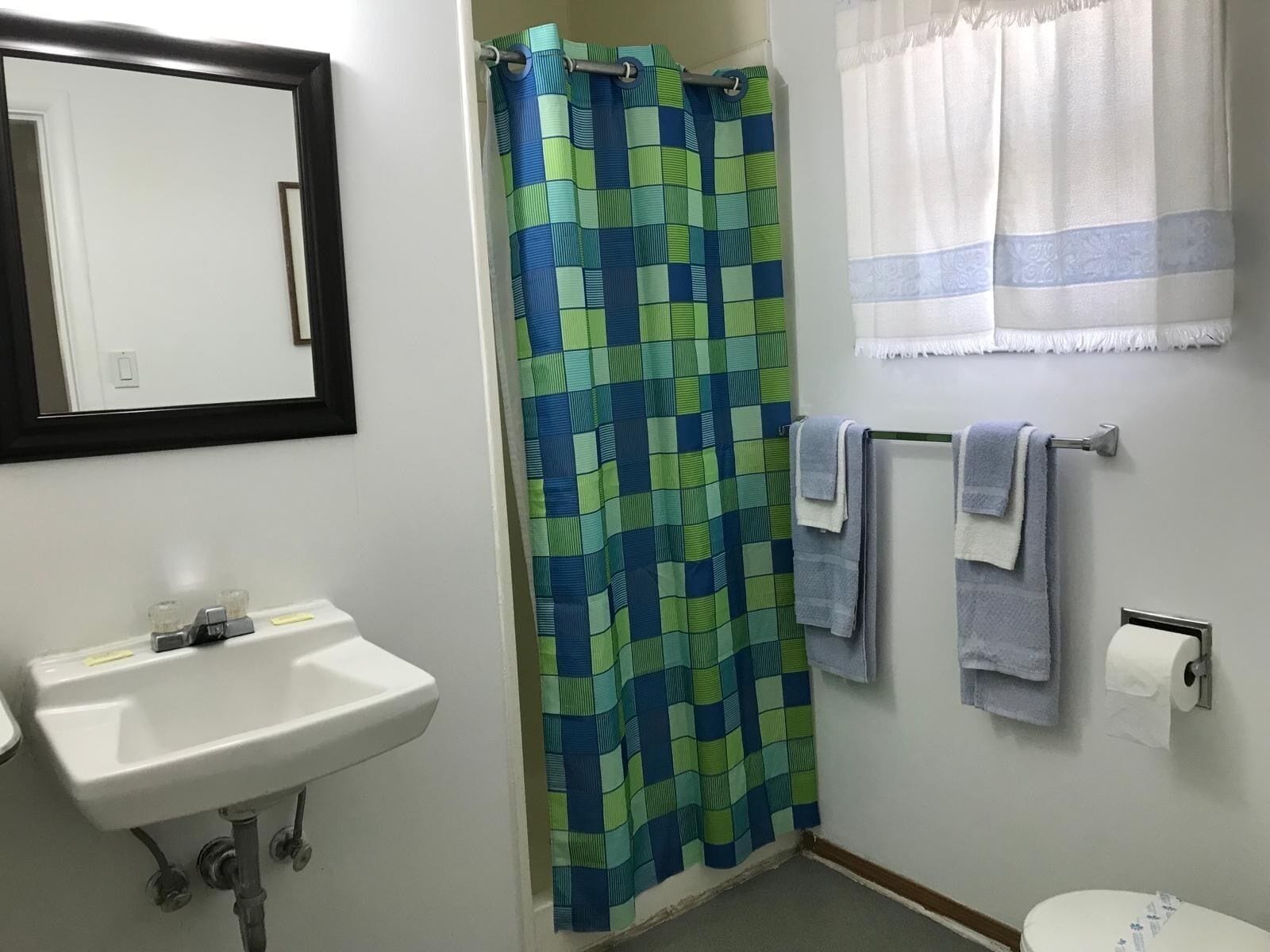 Une salle de bain avec un lavabo blanc, un rideau de douche, un porte-serviettes avec des serviettes et des toilettes.