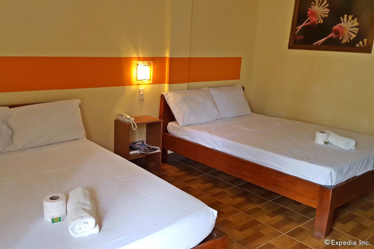 A hotel room with two beds, a nightstand with a phone, and a wall-mounted light.