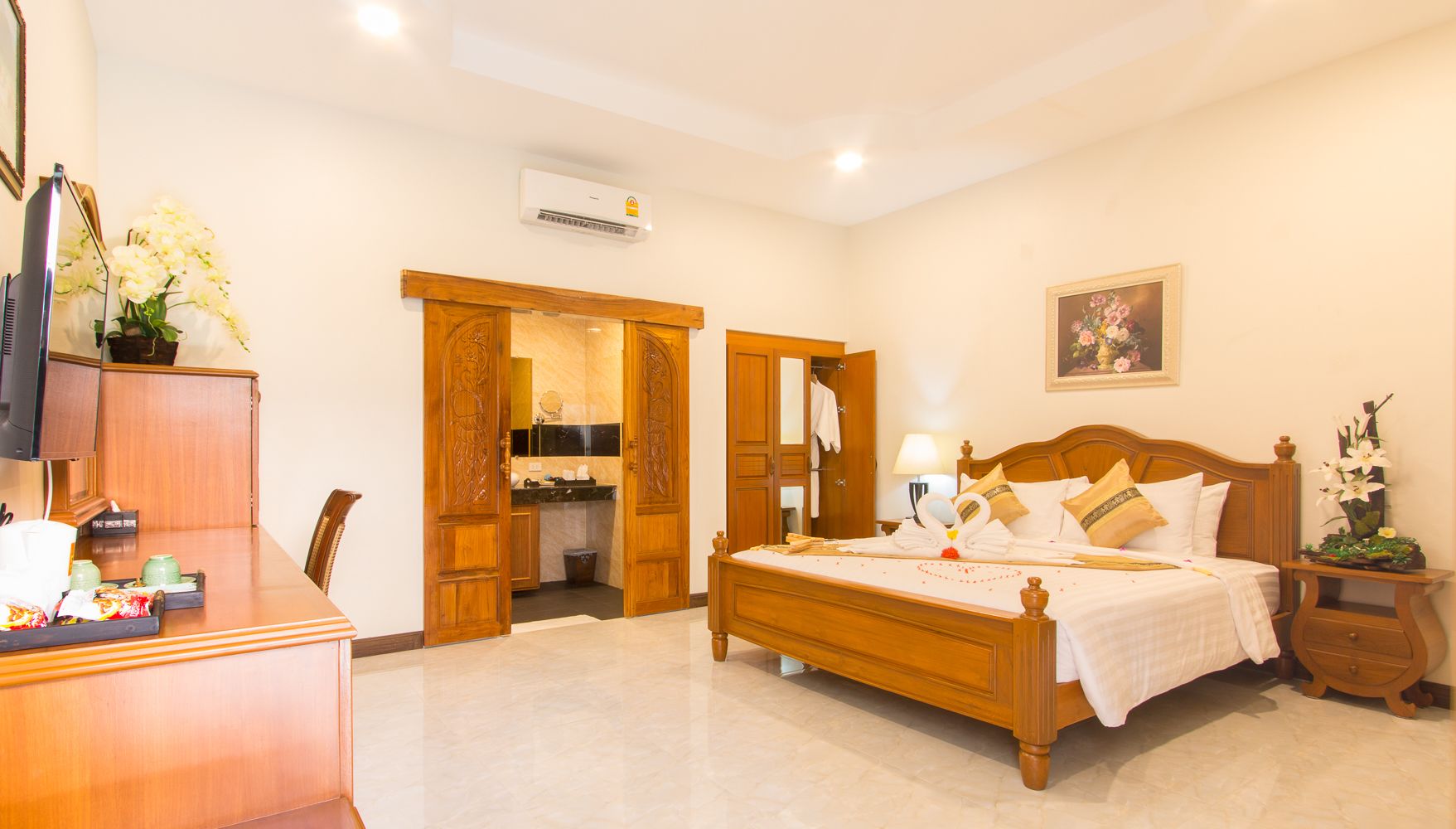 Una camera d'albergo con un letto di legno, una scrivania con un computer, un bagno con uno specchio e un quadro appeso al muro.