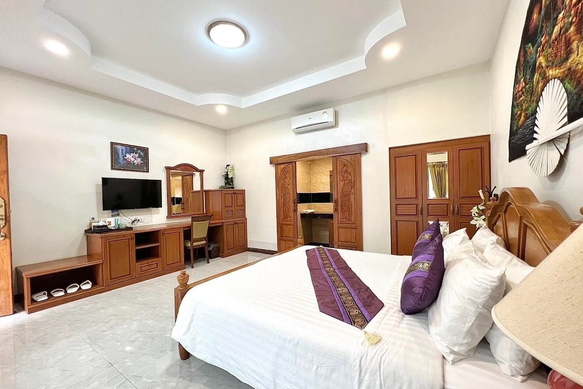 A hotel room with a large bed, a desk with a chair, a television, and a wardrobe.