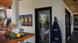 A hotel lobby with a reception desk, a painting of parrots, a water dispenser, and a bookshelf. - Hakuna Matata Bali Villas (Pecatu)