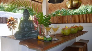 A bar area with a Buddha statue, a potted plant, two drinks, and coconuts. - Hakuna Matata Bali Villas (Pecatu)