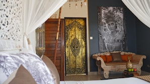 A bedroom with a canopy bed, a wooden door with intricate designs, a sofa with cushions, and a wall-mounted picture. - Hakuna Matata Bali Villas (Pecatu)