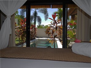 Quarto com vista para uma piscina, rodeado por plantas tropicais.