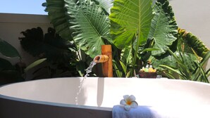 A bathroom with a large sink, a wooden faucet, and a flower on a towel. - Hakuna Matata Bali Villas (Pecatu)