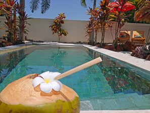 Piscina com bebida decorativa na borda, rodeada por plantas tropicais e pedras.