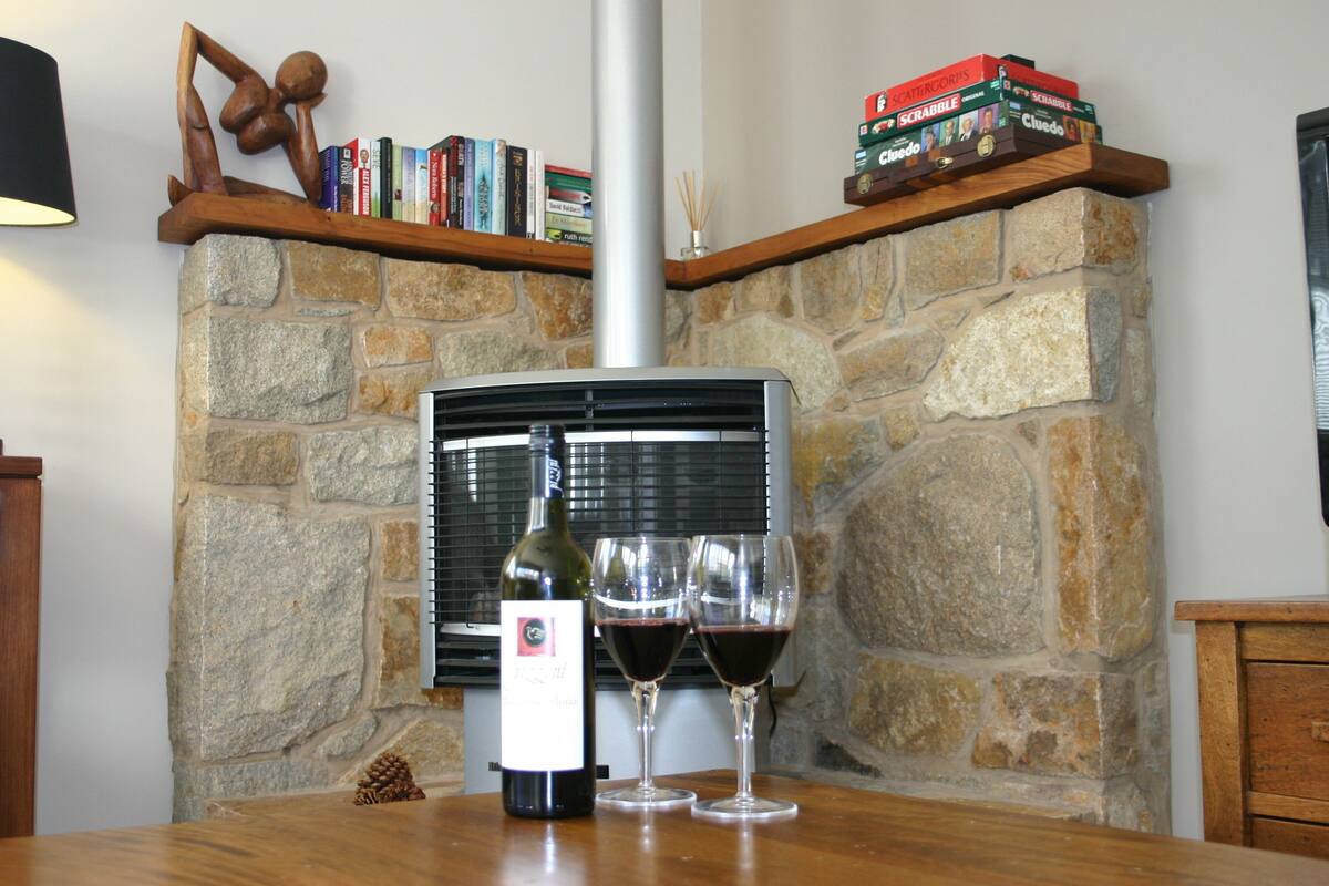 A stone fireplace with a modern heater, a bottle of wine, and two wine glasses on a wooden table.