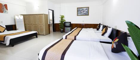 Una habitación de hotel con tres camas, un televisor, una planta y un cuadro en la pared.