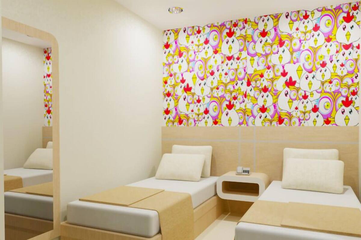 Une chambre d’hôtel avec deux lits, un miroir et un mur décoré de motifs colorés sur le thème des poulets.