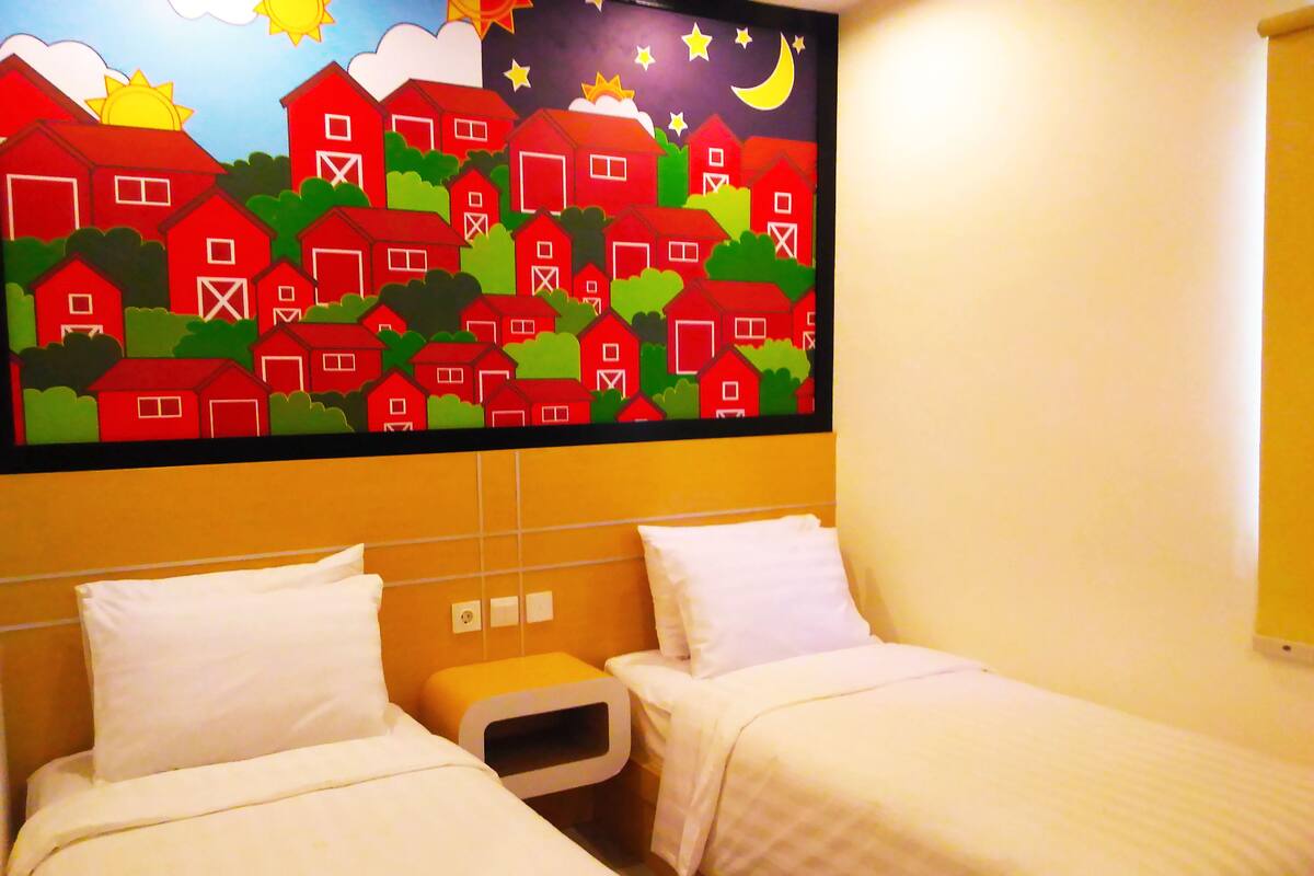 Une chambre d’hôtel avec deux lits, une fresque représentant des granges rouges et des arbres verts, et un ciel nocturne étoilé avec un croissant de lune.