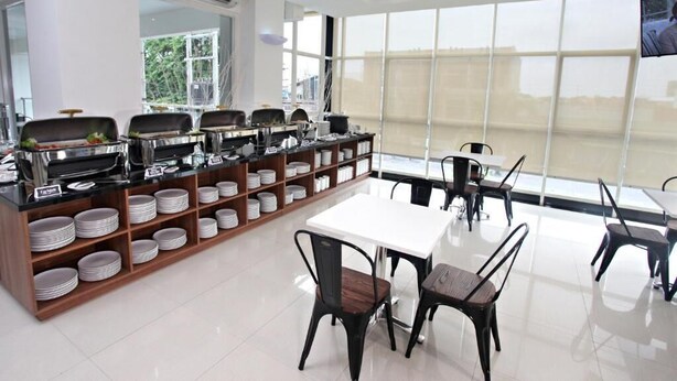 A modern dining area with a buffet setup, white tables, and black chairs. - Nite & Day Surabaya - Gunungsari (Surabaya)
