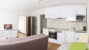 Una cucina moderna con mobili bianchi, un frigorifero in acciaio inossidabile, un forno e un forno a microonde. C'è un'area pranzo con un tavolo verde e una sedia beige.