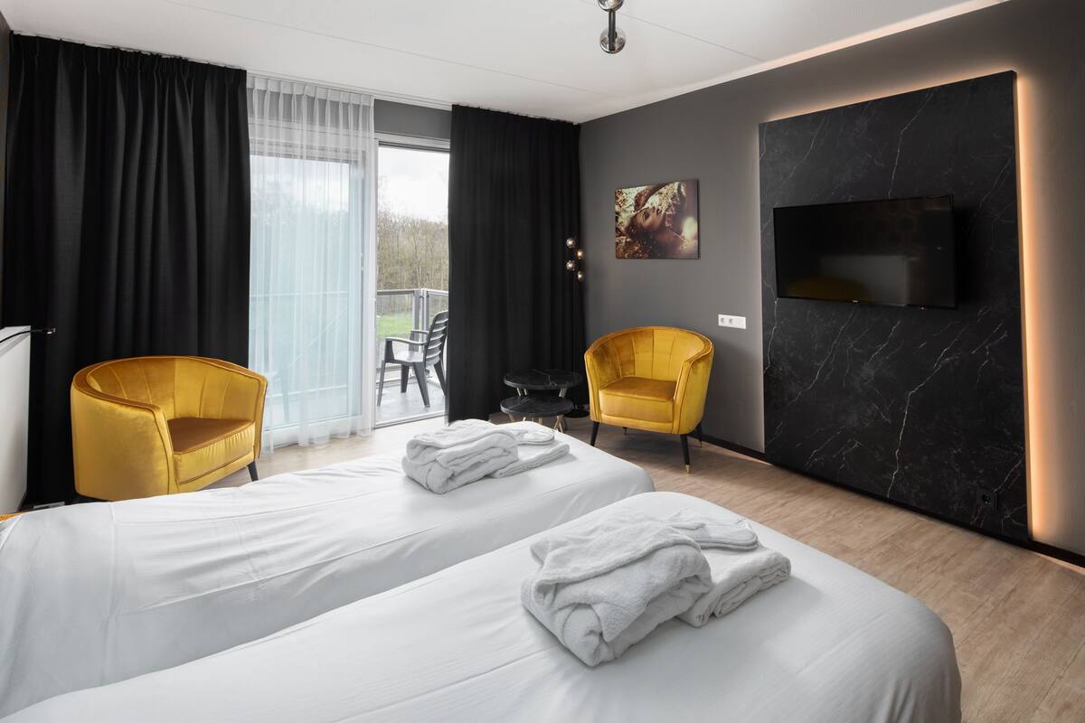 Une chambre d’hôtel avec deux lits, un téléviseur, un tableau et deux chaises jaunes.