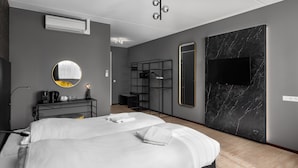 Una habitación de hotel moderna con una cama grande, un televisor montado en la pared, un espejo y un pequeño escritorio con lámpara.