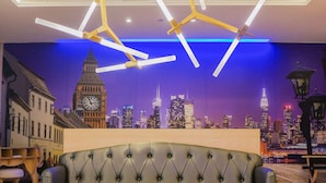 A modern living room with a tufted sofa, a round coffee table, and a cityscape mural on the wall.