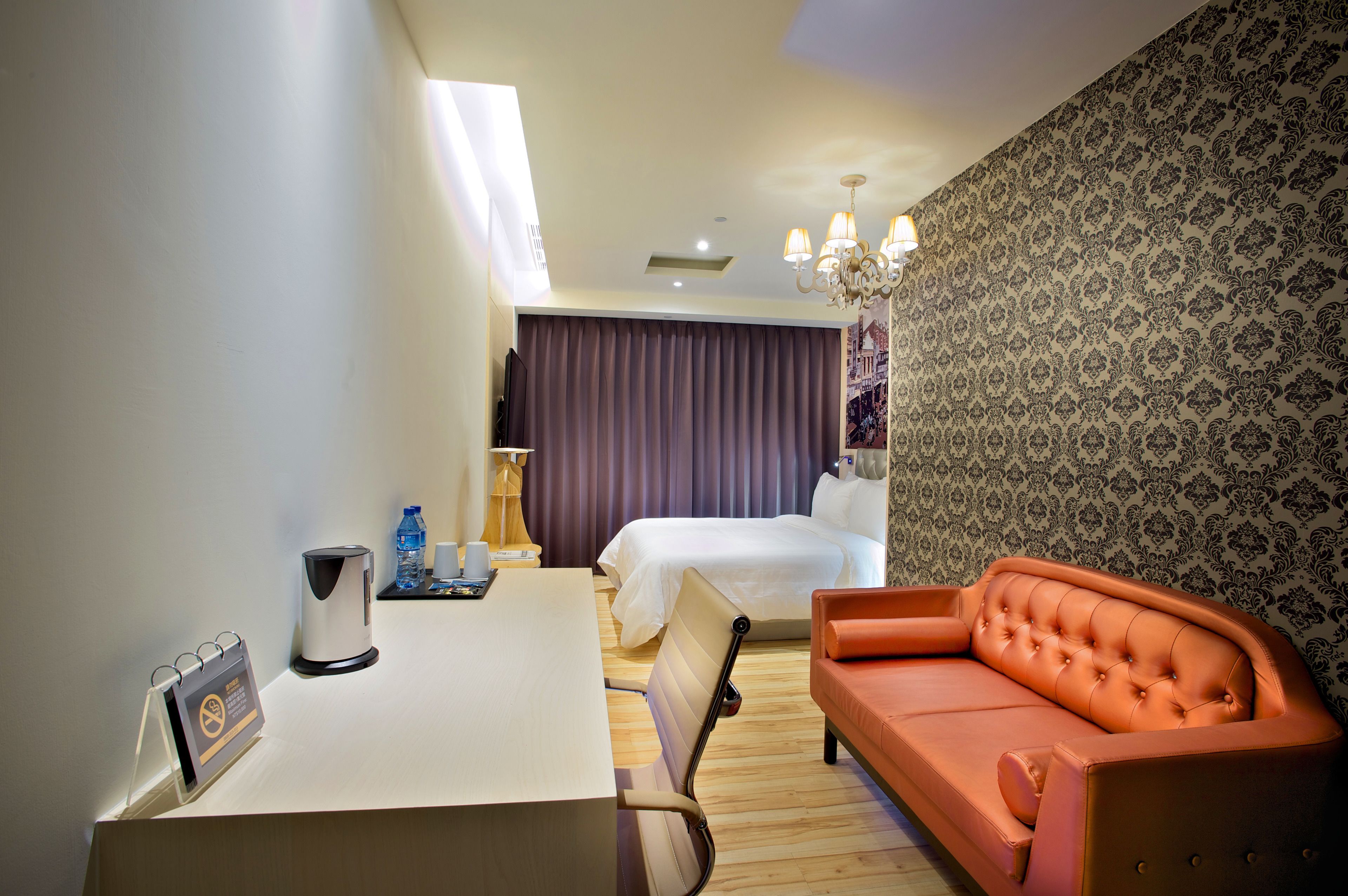 A hotel room with a bed, a sofa, a table with a coffee maker, and a wall with patterned wallpaper.
