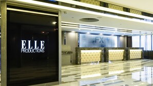 A lobby with a reception desk, a large 'ELLE PRODUCTIONS' sign, and a polished marble floor.