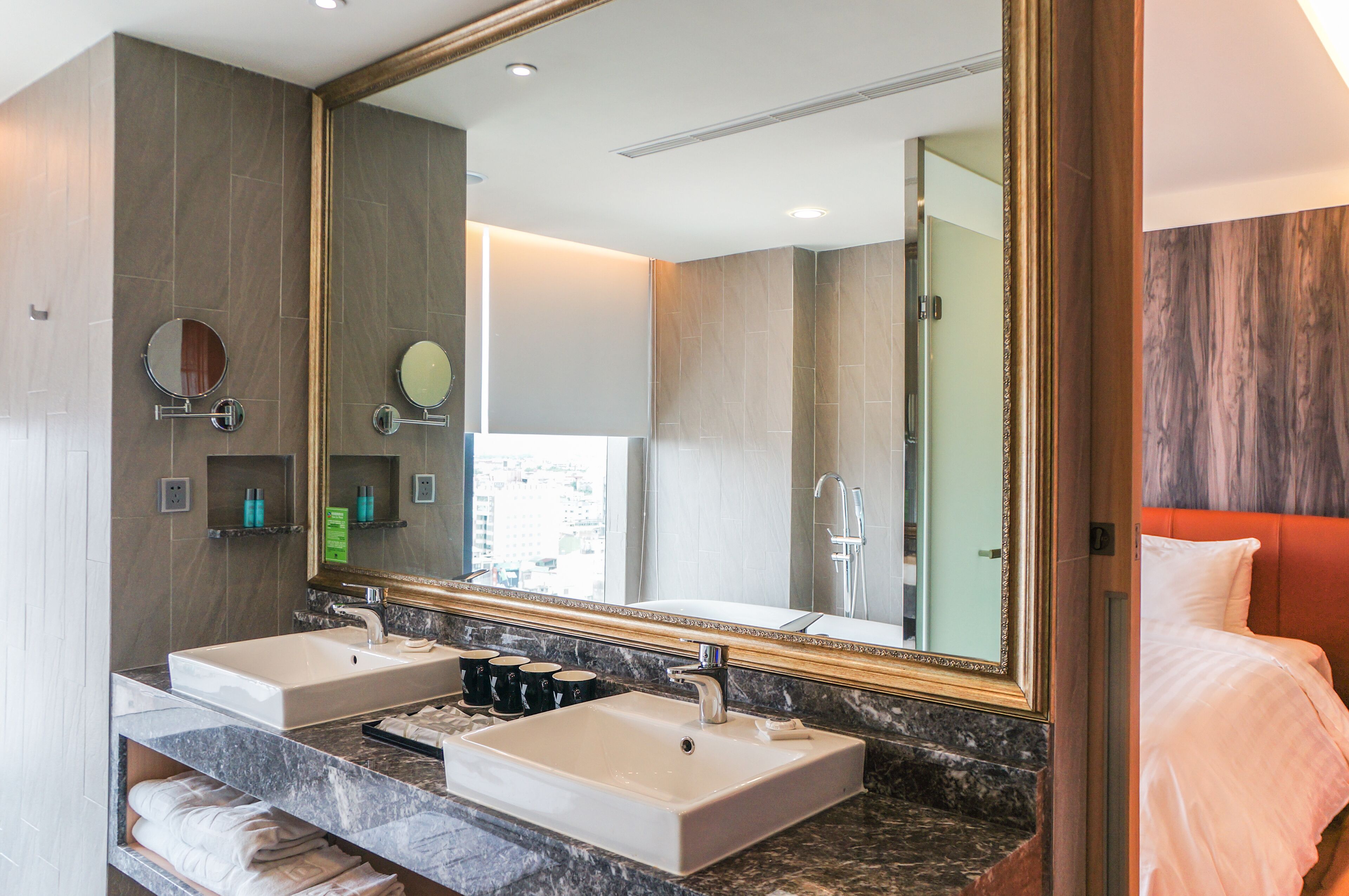 Une salle de bain moderne avec deux lavabos, un grand miroir et un lit doté d’une tête de lit rouge.