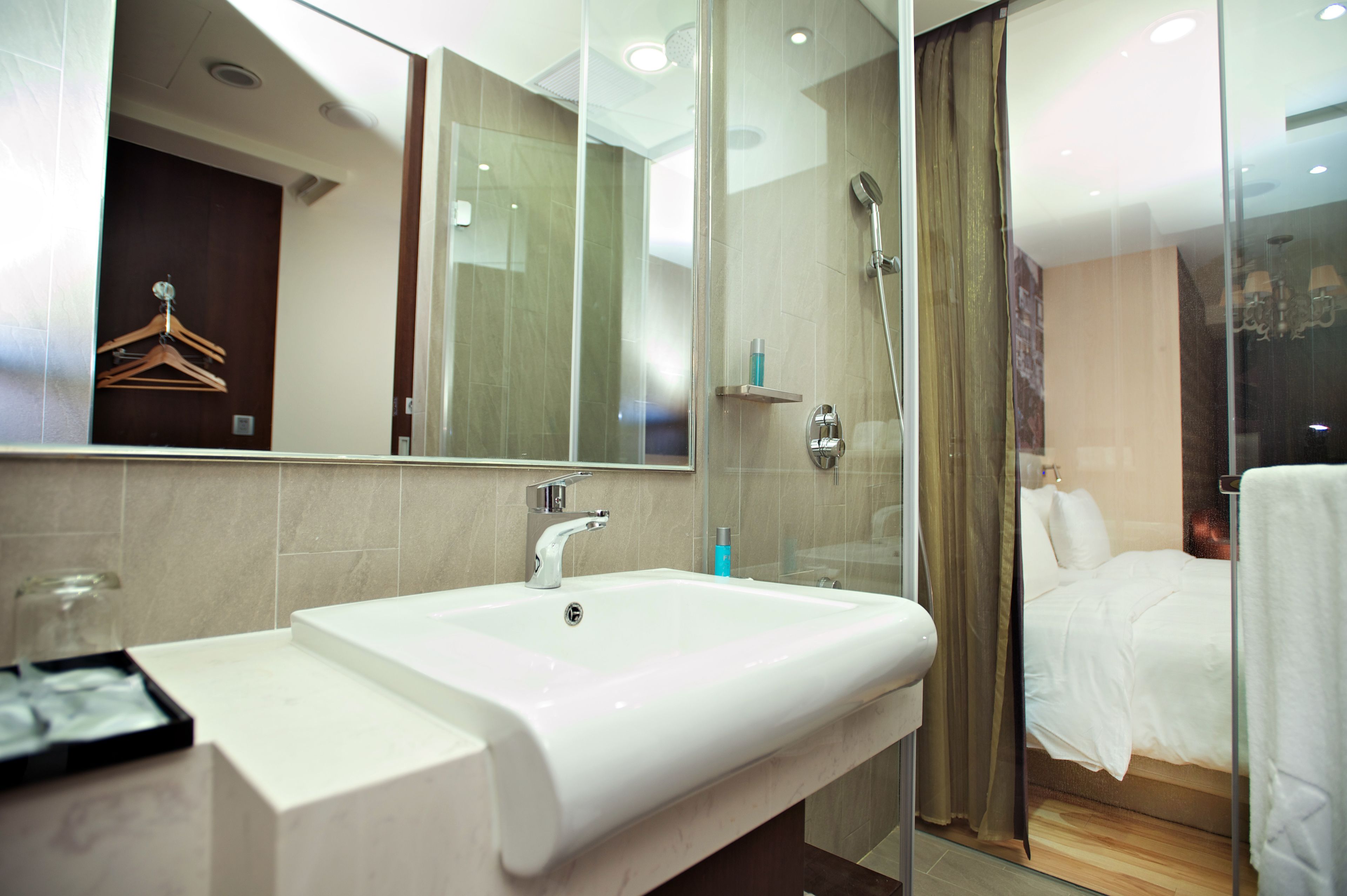 A modern bathroom with a white sink, a glass shower enclosure, and a bed with white linens.