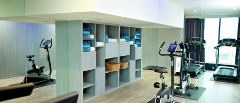 A modern gym with cardio equipment, water bottles, and storage shelves.