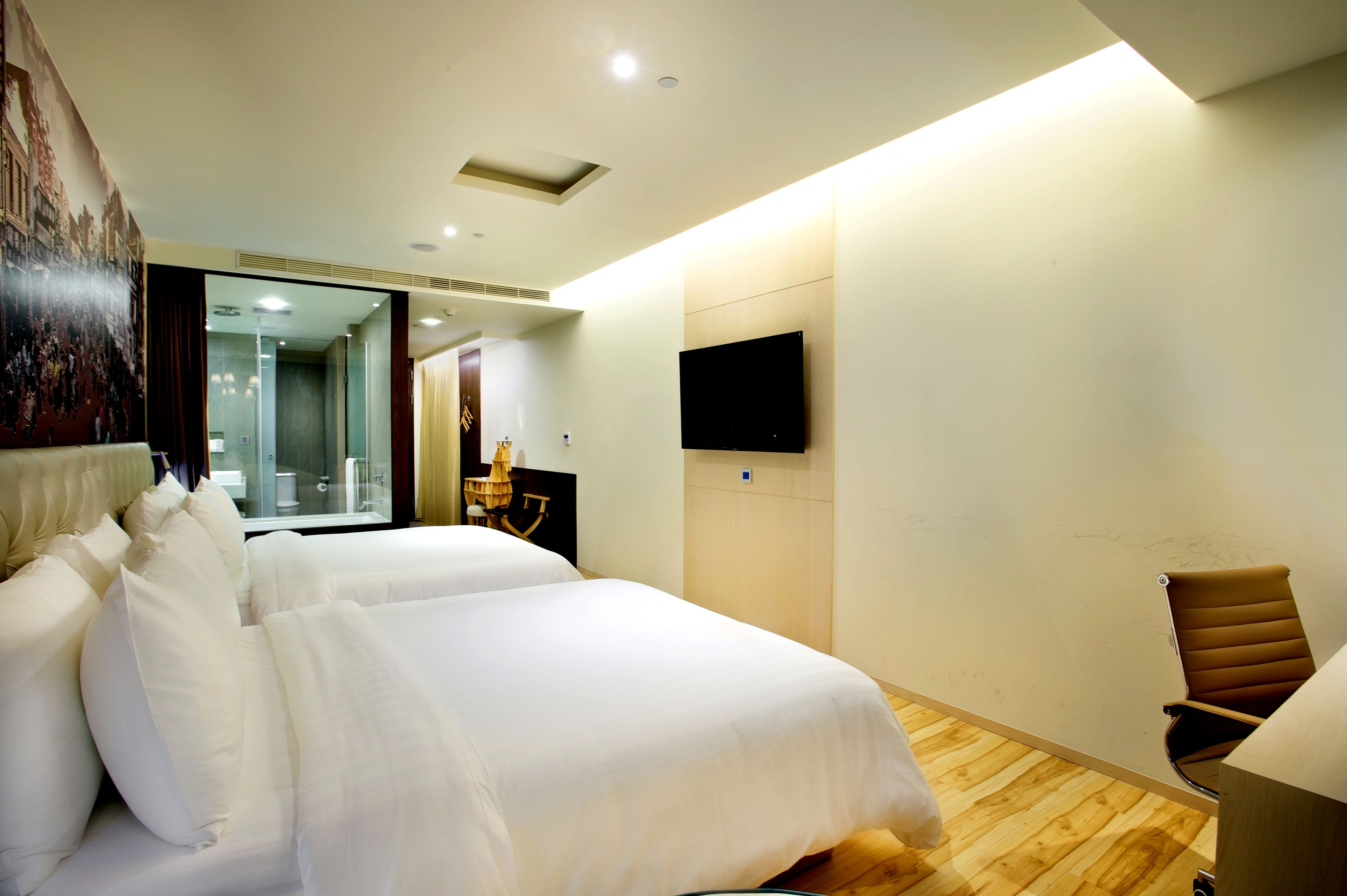 A hotel room with two beds, a flat-screen TV mounted on the wall, and a wooden floor.
