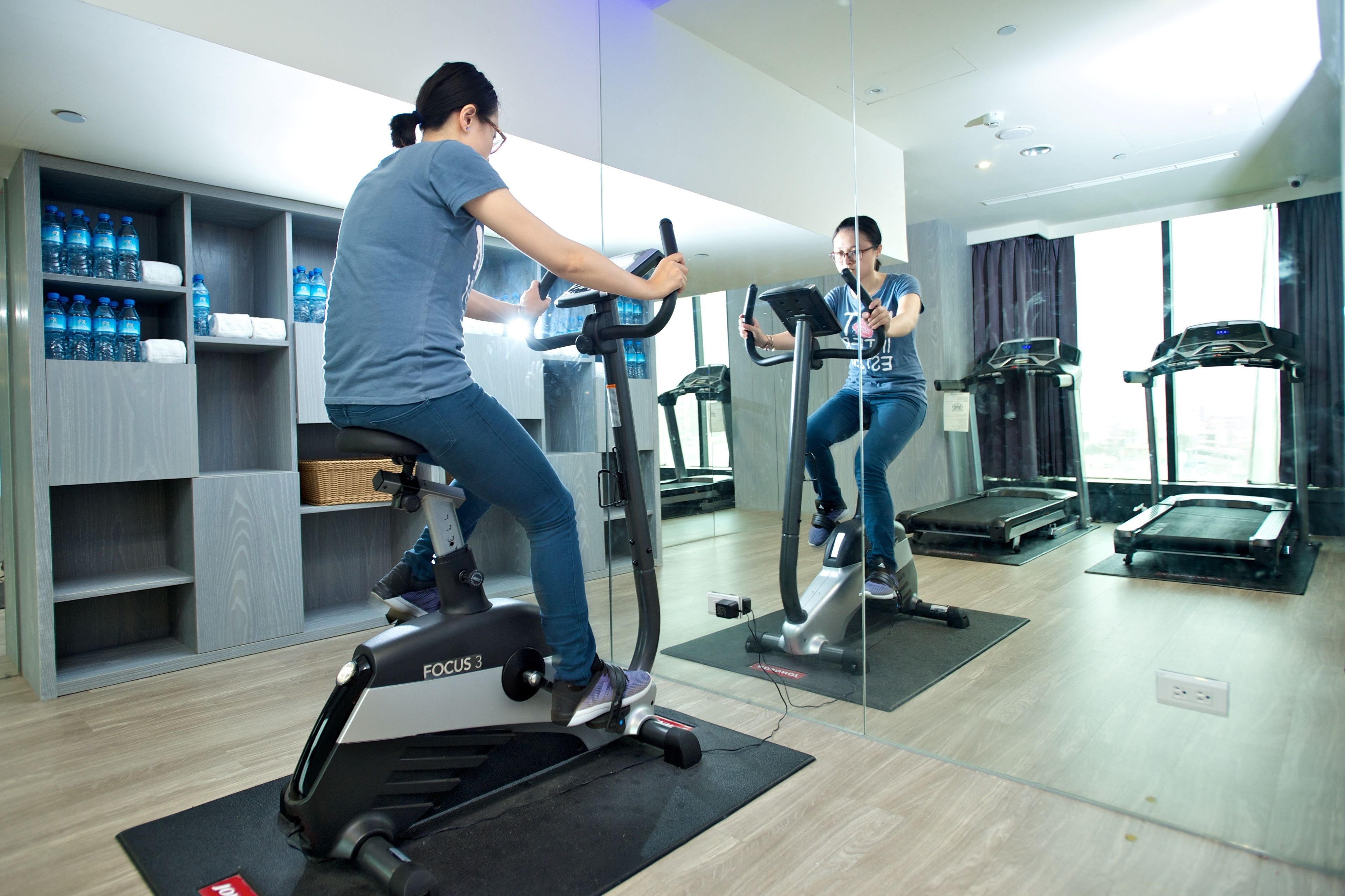 A gym with cardio equipment, a water station, and a mirror reflecting the room.