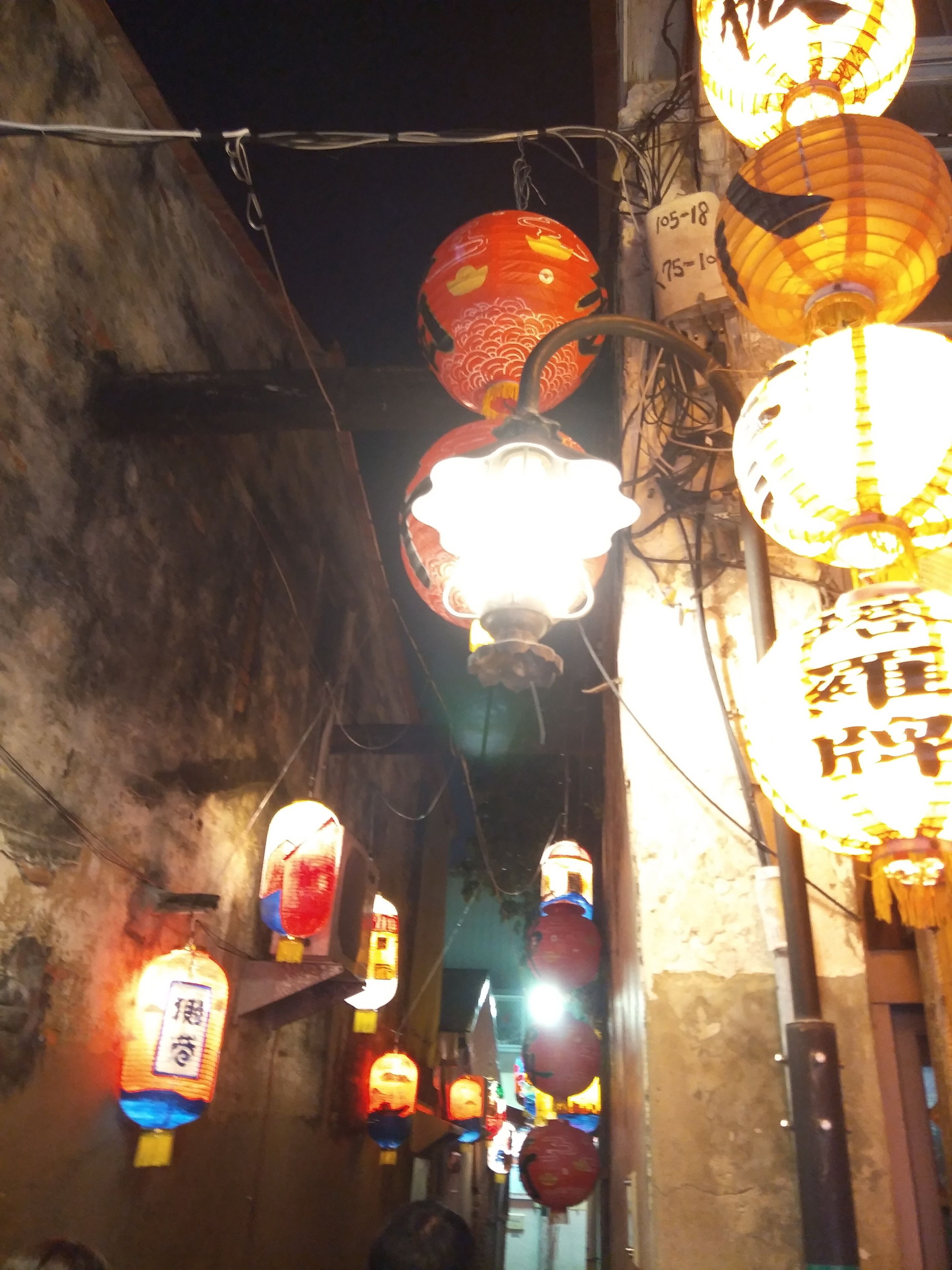 A narrow alleyway with traditional lanterns hanging overhead.