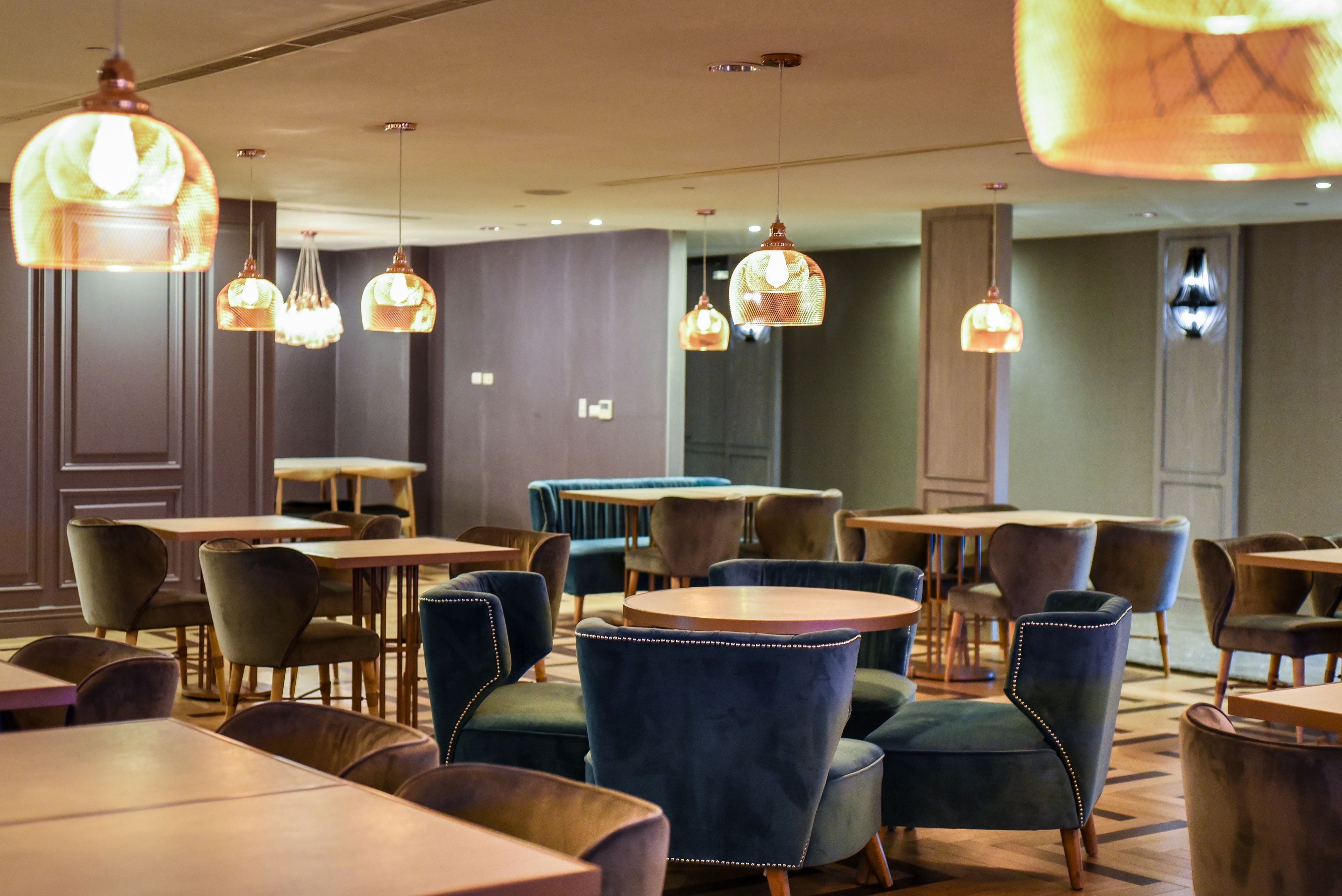 A restaurant with round tables and velvet chairs, featuring pendant lighting.