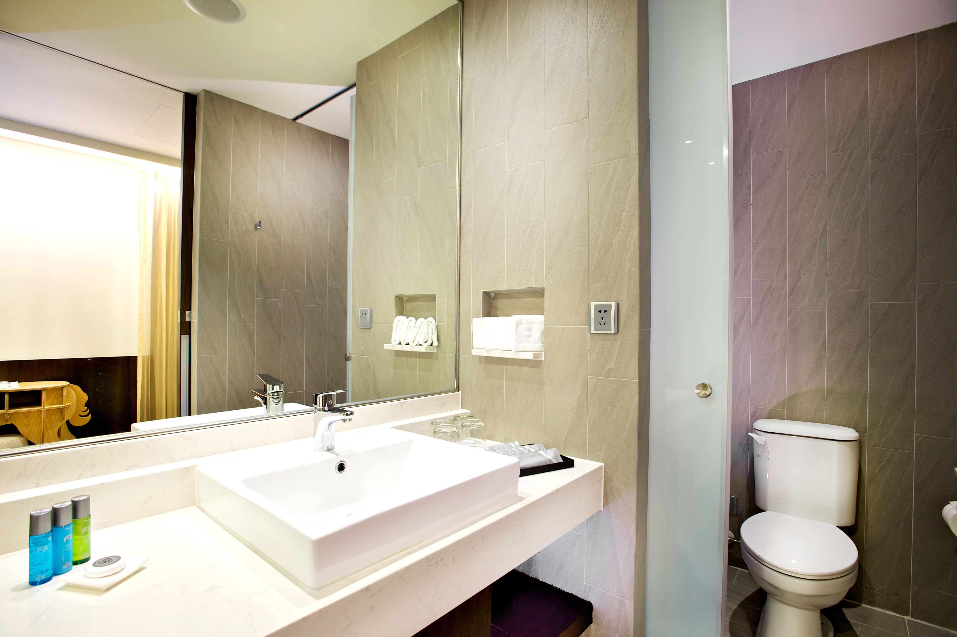 Un baño moderno con un espejo grande, un lavabo blanco y un inodoro.