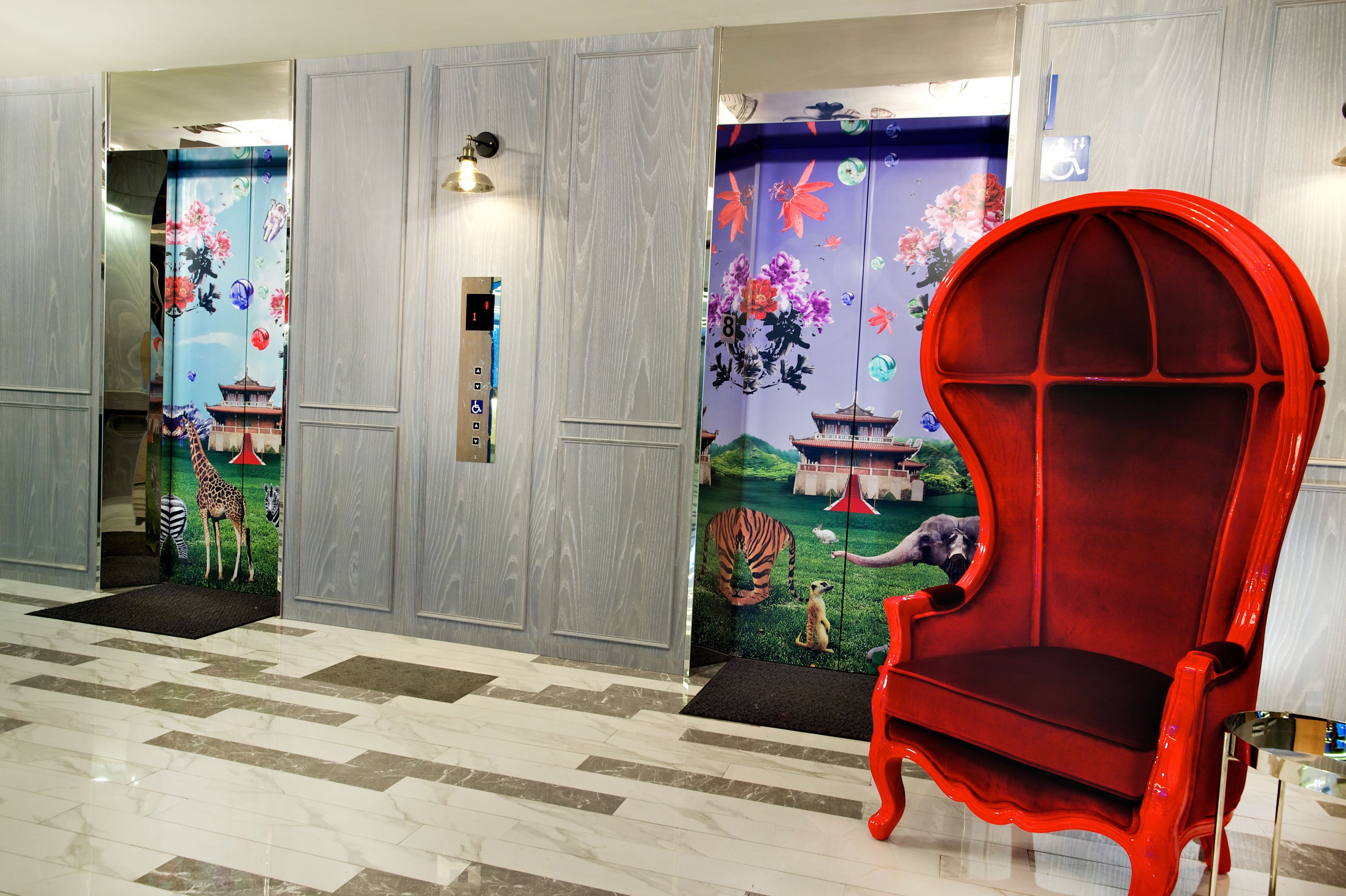 Eine Lobby mit einem roten Sessel, einem Aufzug und einer Wand mit Tier- und Floralmotiven.