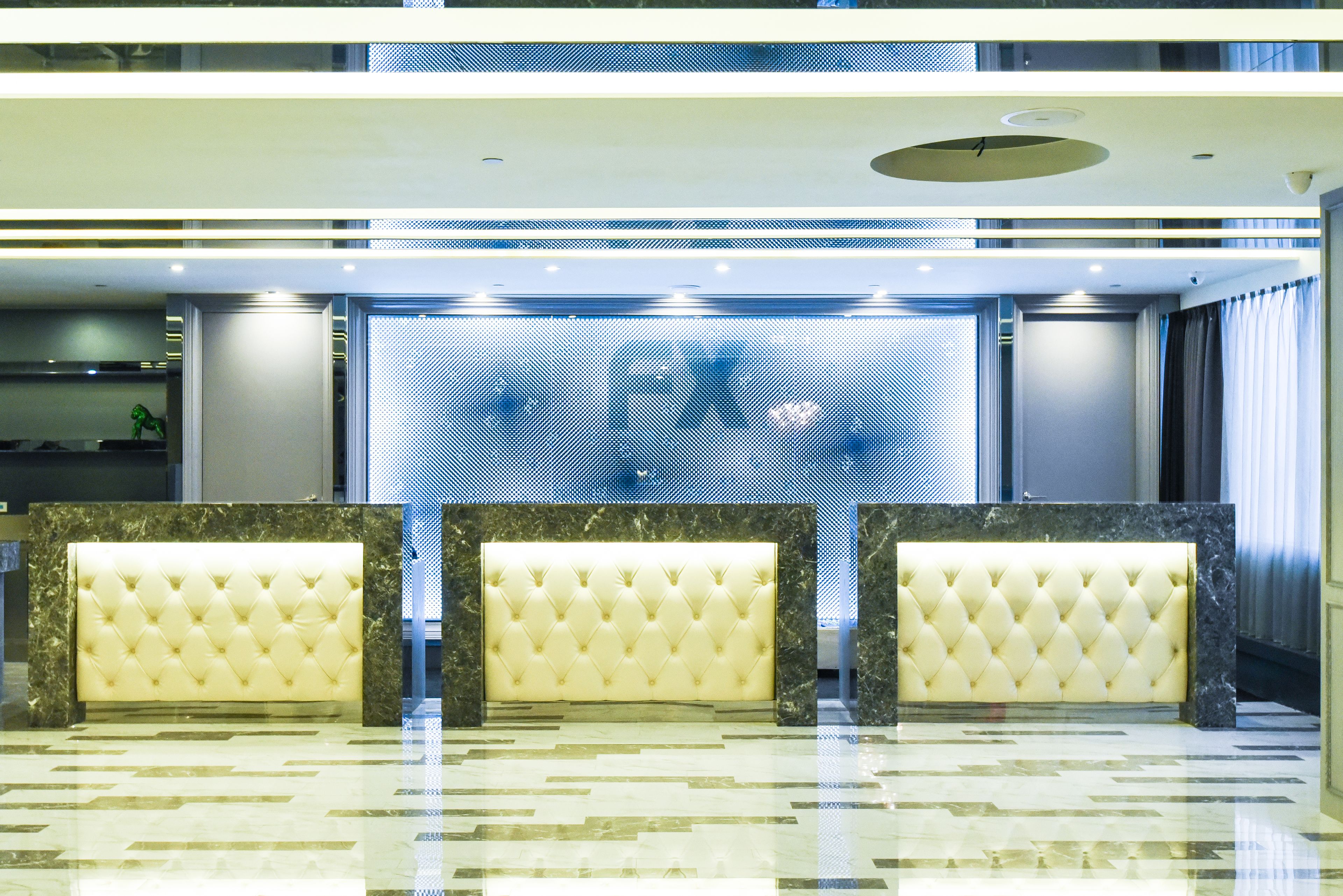 A lobby with three plush, cream-colored sofas arranged in a row, a large digital screen displaying a blurred image, and a polished marble floor.