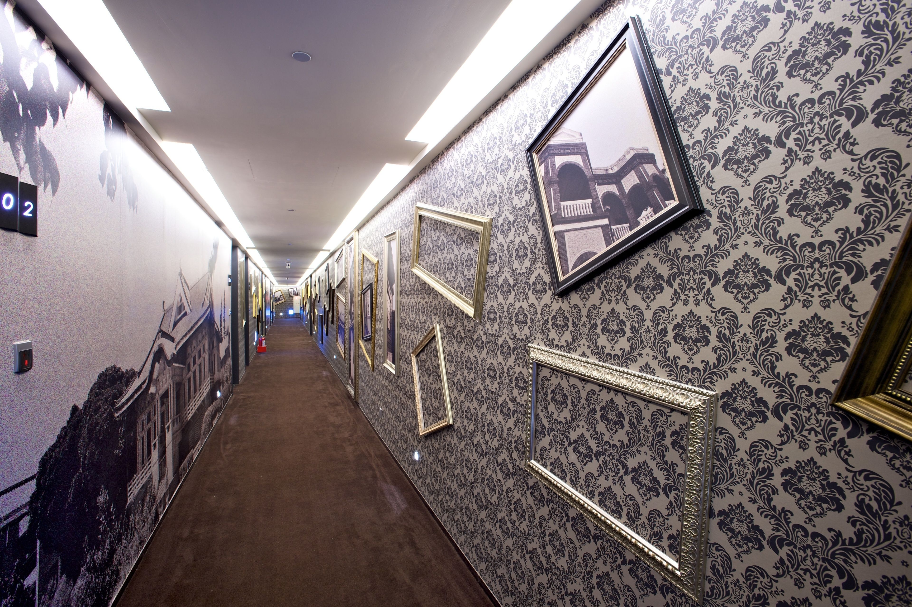 A hallway with patterned wallpaper and framed pictures on the walls.