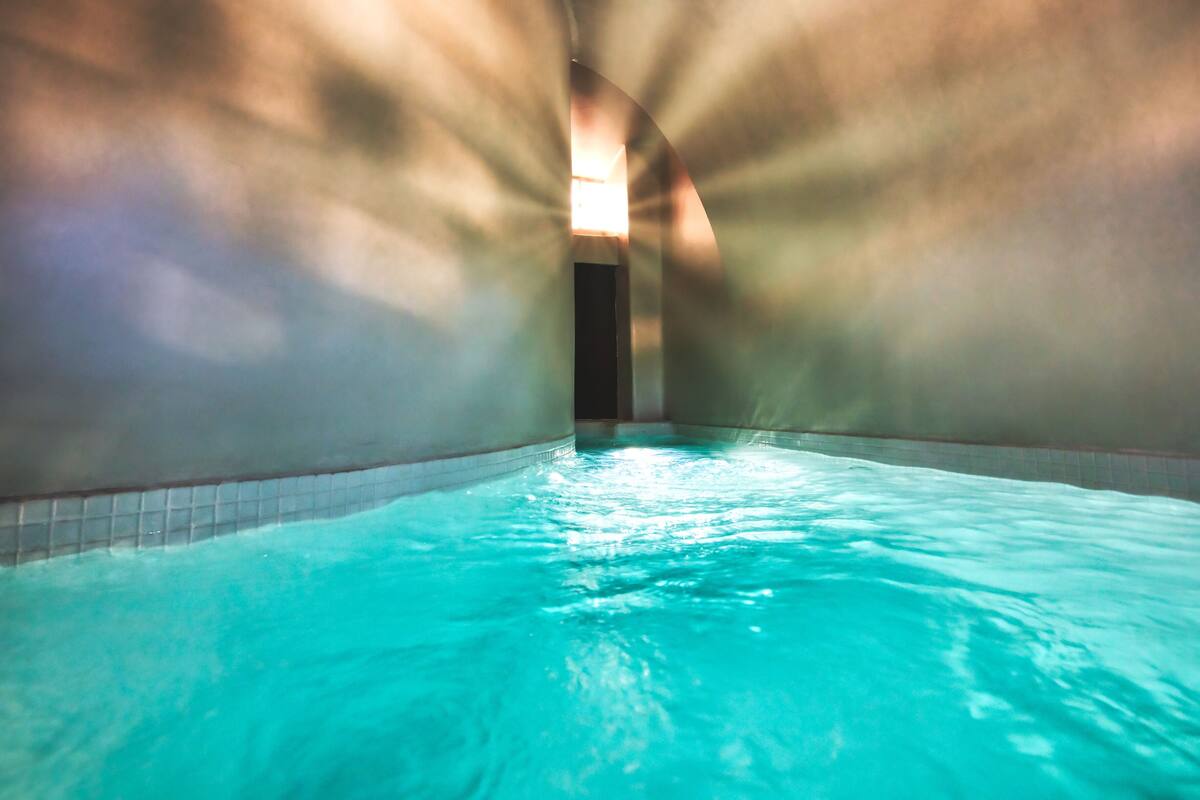 An indoor swimming pool with clear water, surrounded by walls with a tiled pattern.