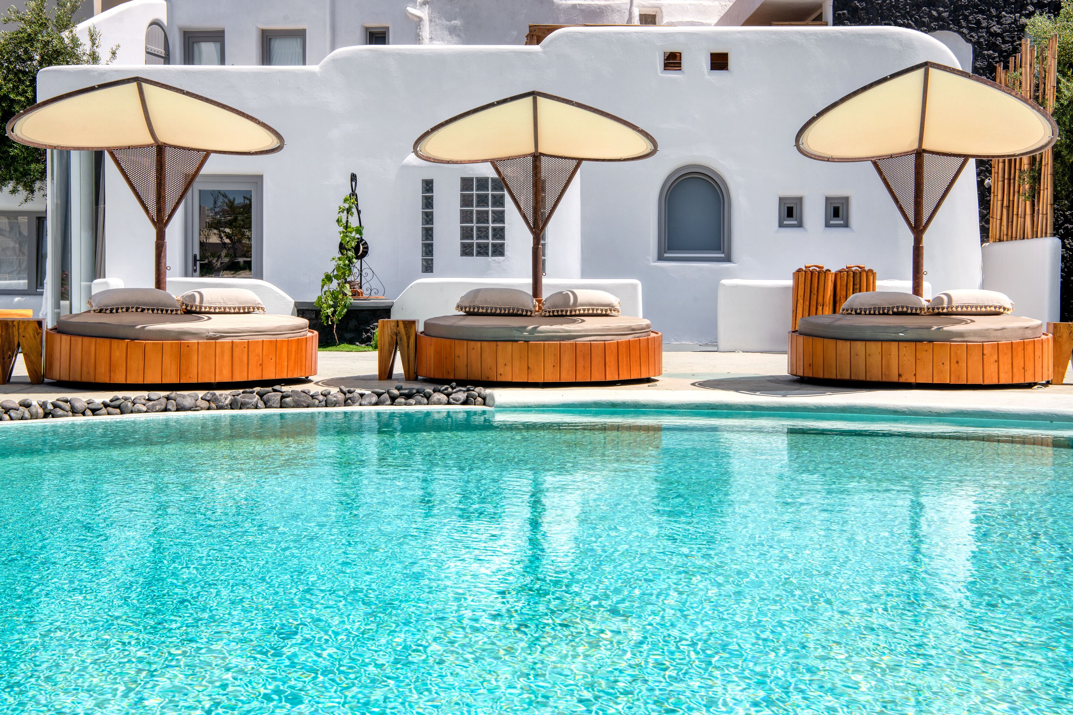 A poolside area with three wooden loungers, each with a beige cushion and a large umbrella.