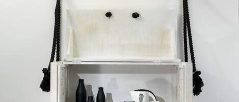 Un meuble blanc en bois, doté de poignées en corde noire, sur lequel sont posés une machine à café et des tasses noires.