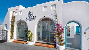 A white building with a 'CALM Collection' sign, arched windows, and a blue door. - San Marino Suites by Calm Collection (Santorini)