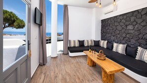 A modern living room with a stone wall, a wooden bench, and a black sofa with patterned cushions. - San Marino Suites by Calm Collection (Santorini)