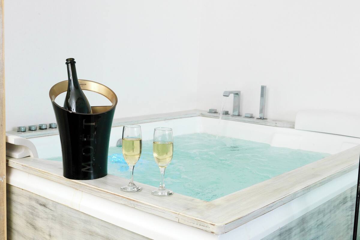 A hot tub with two glasses of champagne and a bottle in a gold bucket.