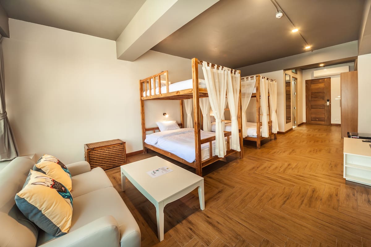 Una habitación de hotel con literas, un sofá, una mesita y suelo de madera.