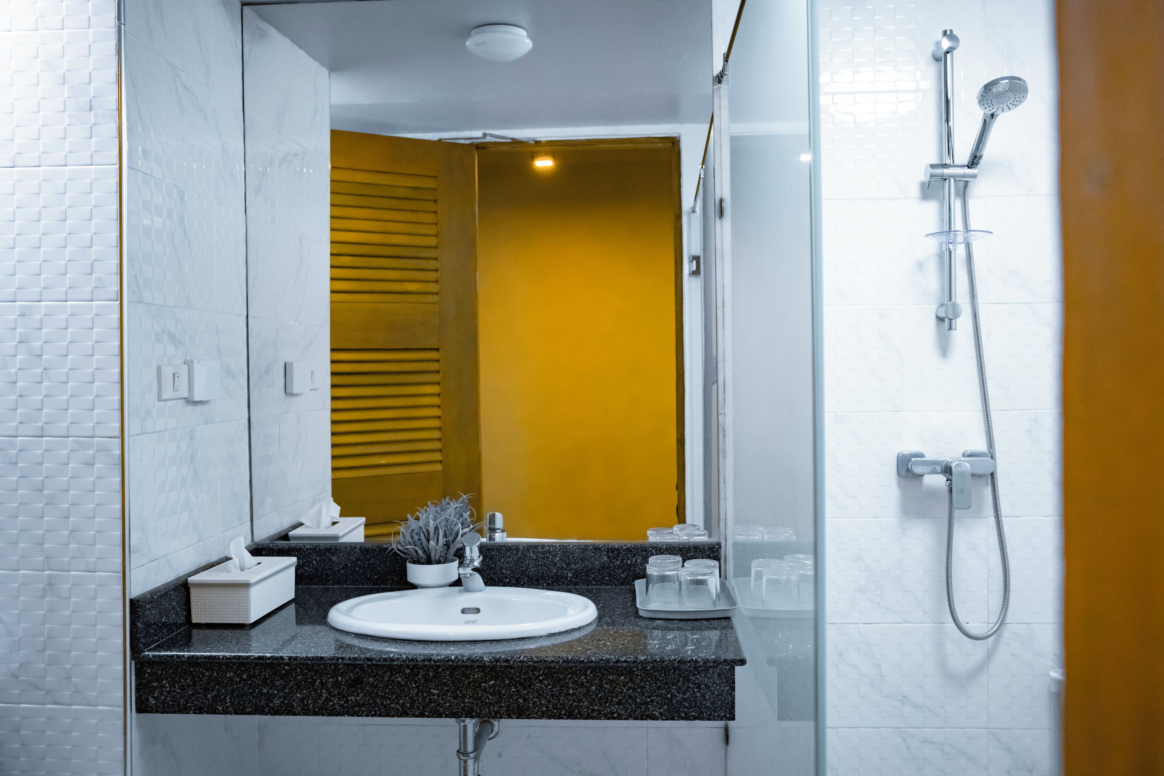 Uma casa de banho moderna com uma pia branca, um espelho, chuveiro e uma porta amarela.