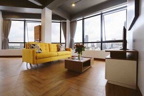 Un salon moderne avec un canapé jaune, une table basse en bois et un meuble blanc. De grandes fenêtres offrent une vue sur le paysage urbain.