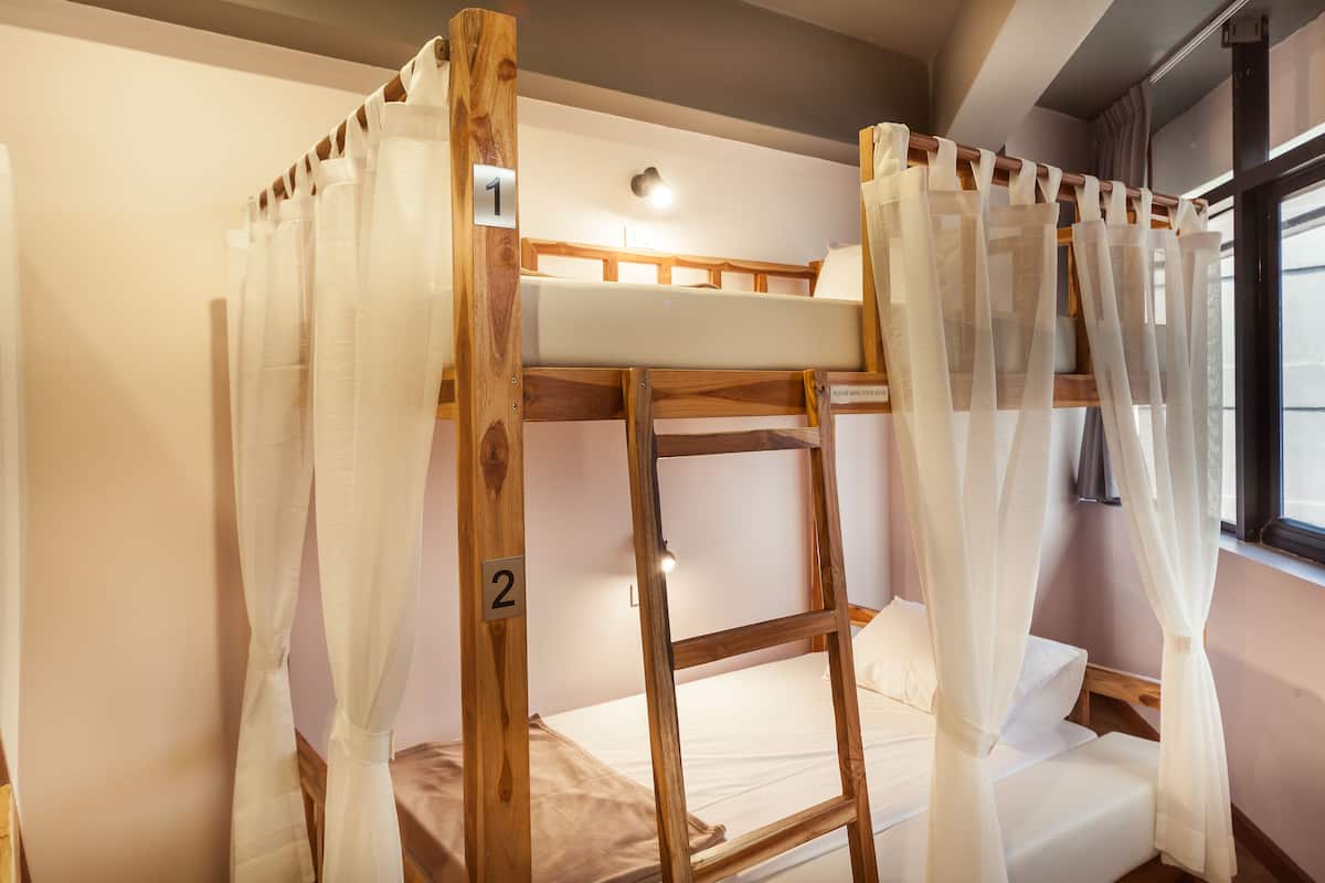 Una cama litera con estructura de madera, ropa de cama blanca y cortinas traslúcidas.