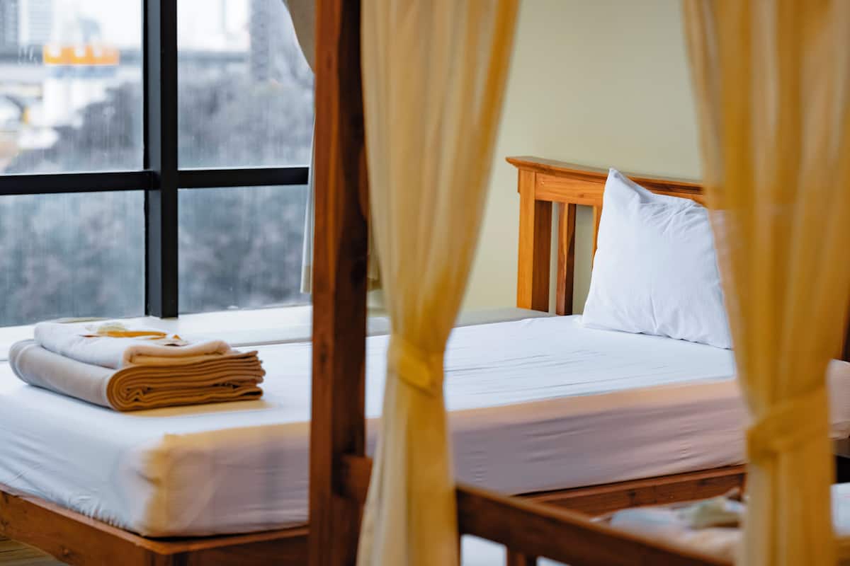 Una cama con sábanas blancas, cabecera de madera y ventana con cortinas.