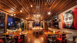 A modern restaurant with wooden ceiling slats, round tables, and red chairs.