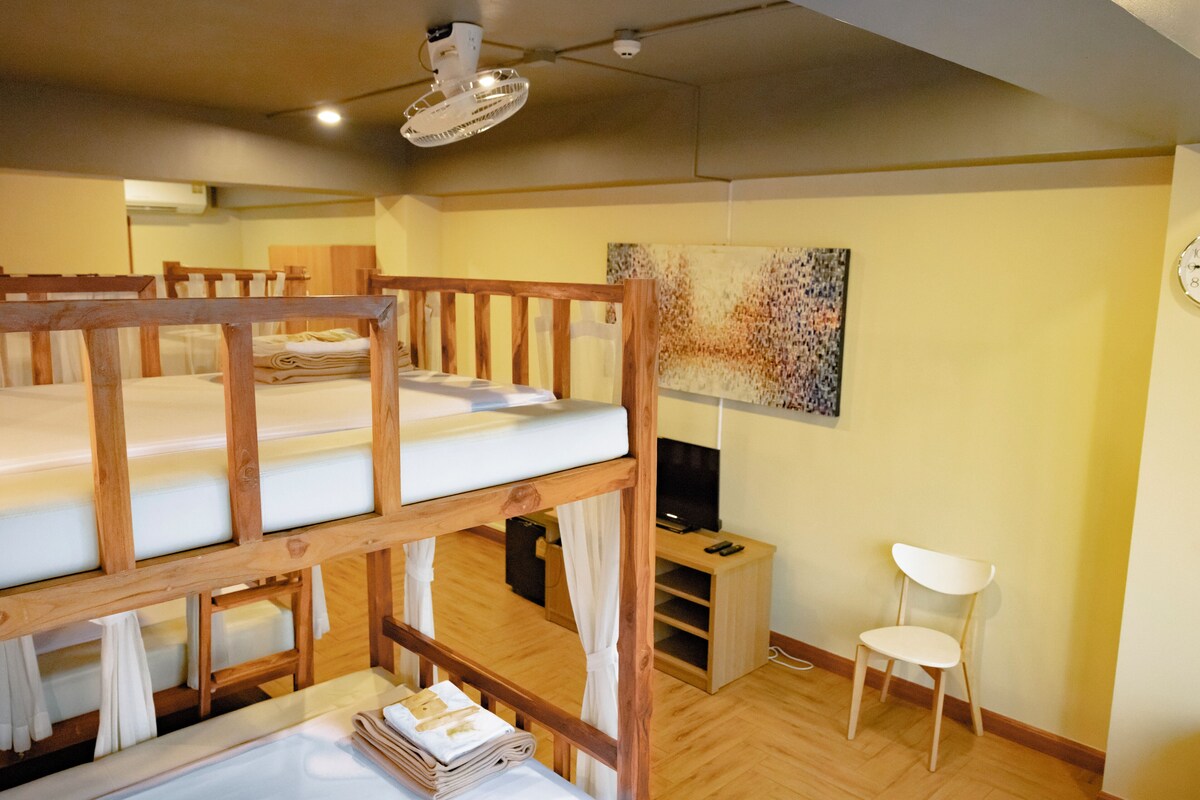 Une chambre avec des lits superposés, un bureau avec un ordinateur, une chaise et un tableau accroché au mur.