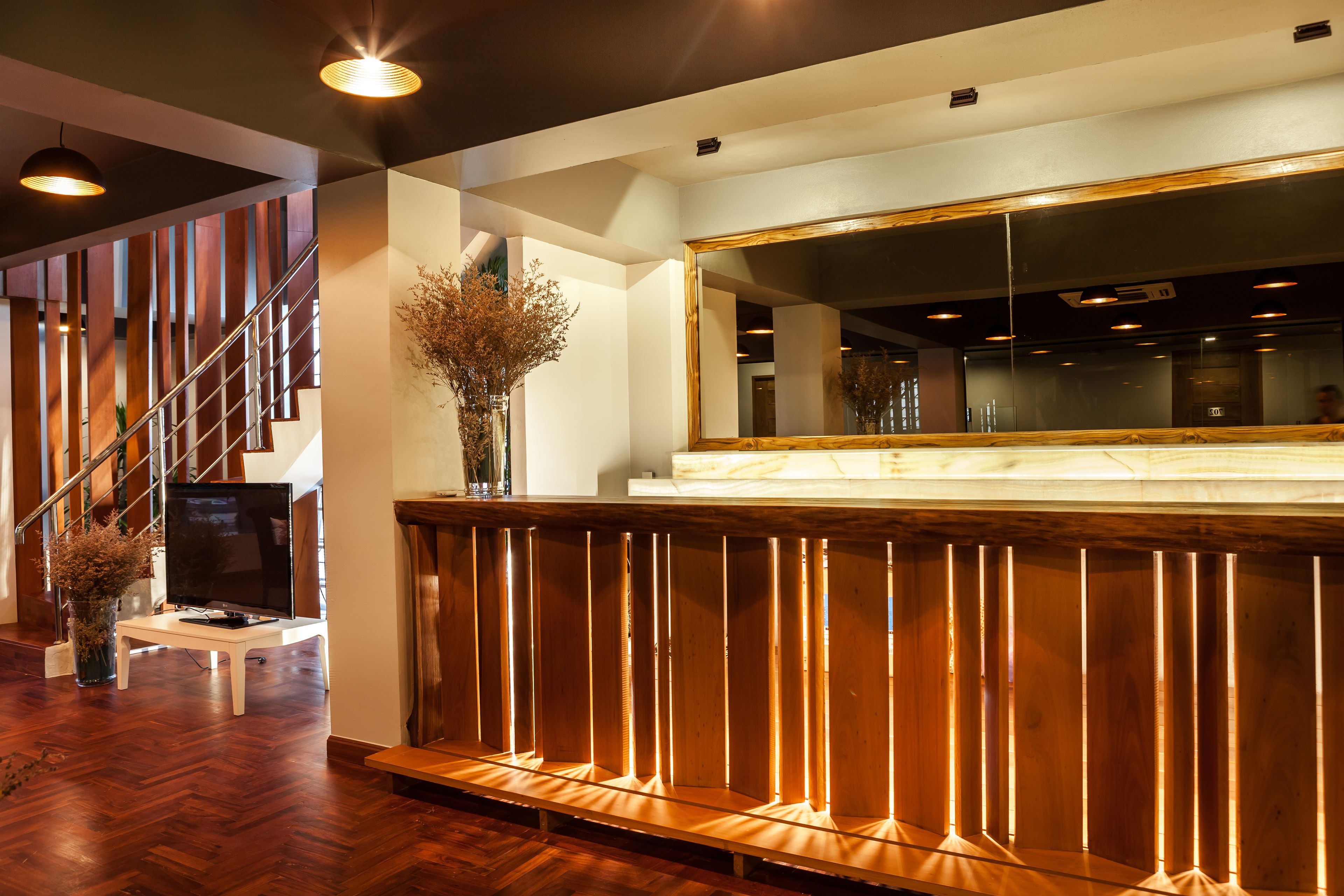 A modern reception area with a wooden reception desk, a large mirror, and a staircase in the background.