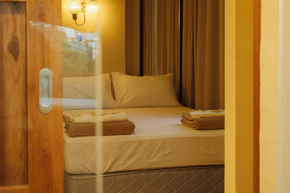 Habitación de hotel con cama, cortinas y una lámpara fijada a la pared.