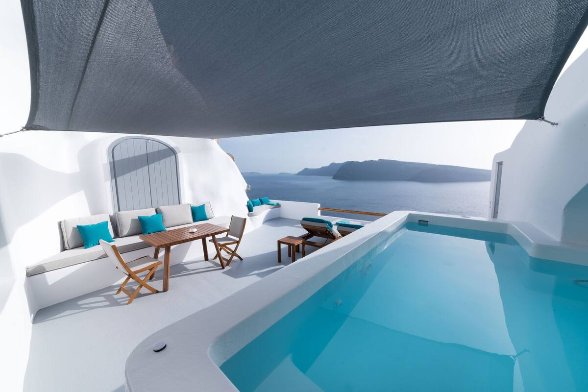 Un espacio al aire libre iluminado por el sol, con piscina, mobiliario y vistas al mar.